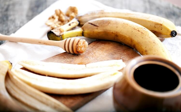 banany na drewnianej desce i szpatułka do nakładania miodu